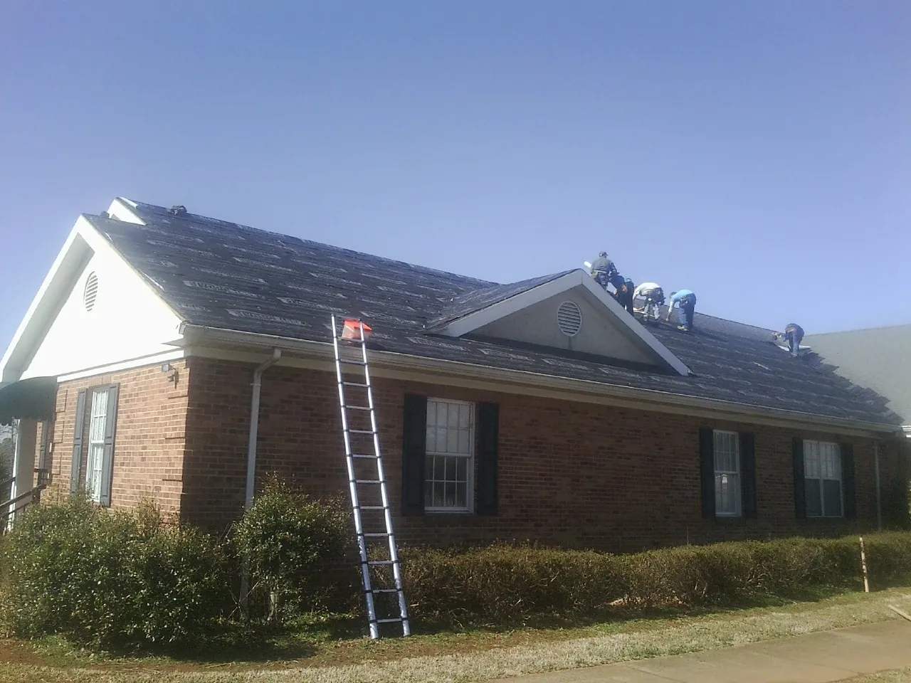 Crew tearing shingles off a brick ranch roof with a ladder set — Metal Roof Repair work by our crew in Croton On Hudson