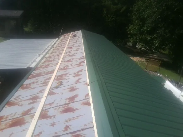Old rusted panels beside newly installed green metal roofing — Wind Damage Roof Repair by Roofing Brothers in Croton On Hudson
