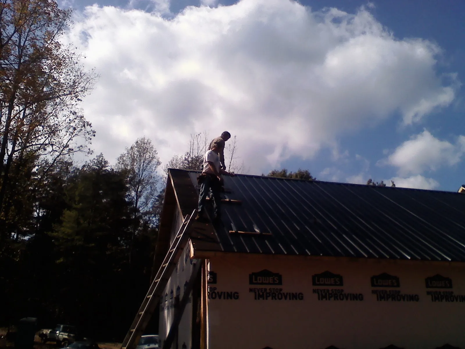 Roofer fastening dark metal panels high against a cloudy sky, from a Roof Inspection job in Croton On Hudson