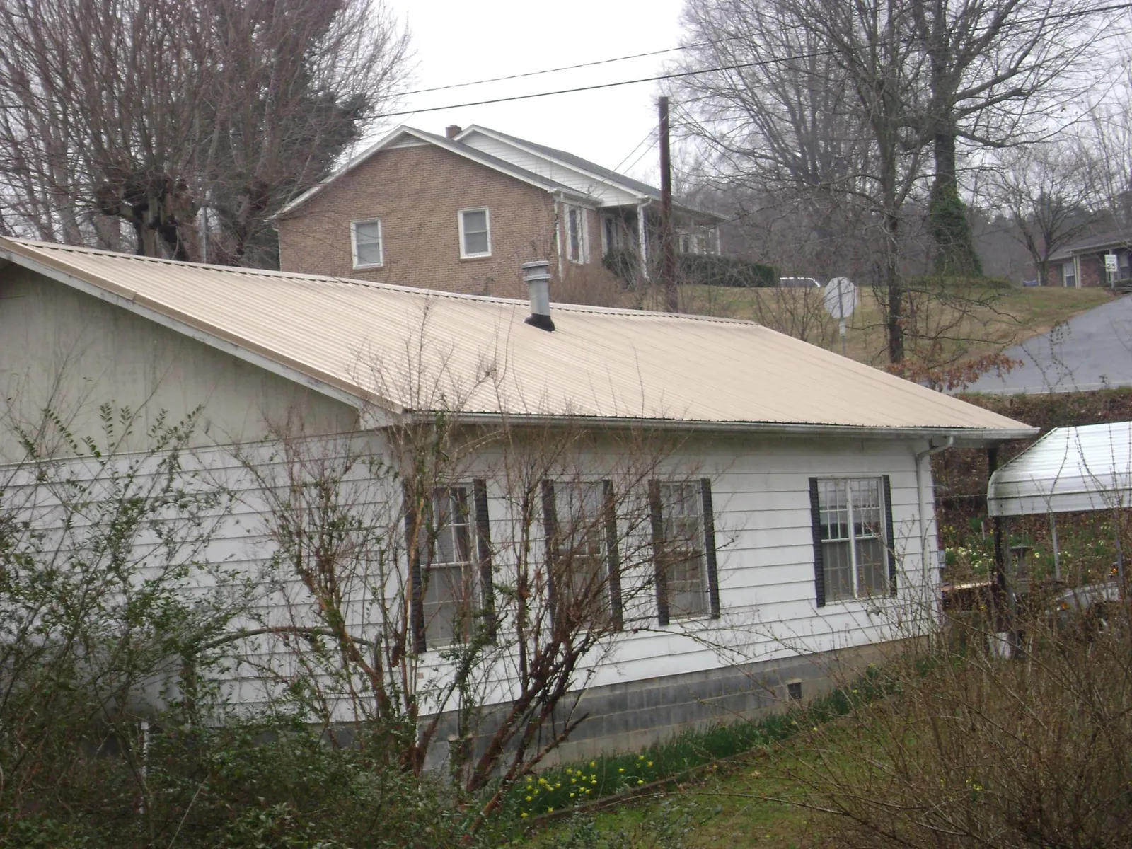 Tan metal roof on a white sided house set into a hillside — Commercial Roofing by Roofing Brothers in Croton On Hudson